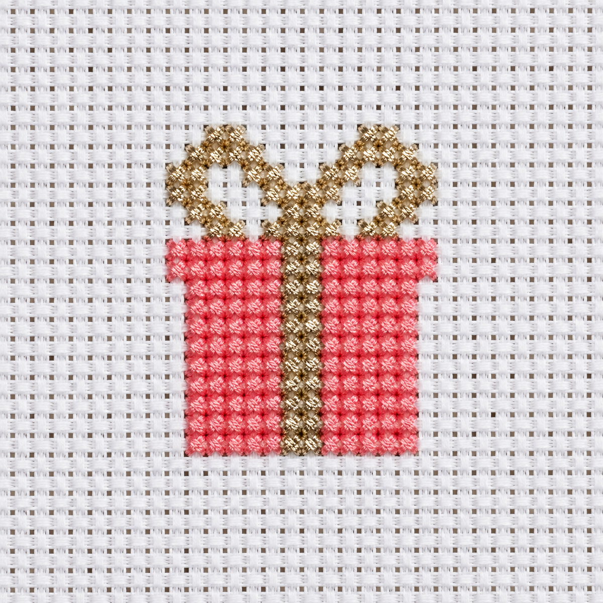 A close-up of a cross-stitch design depicting a red gift box with a gold ribbon and bow, stitched on white mesh fabric.