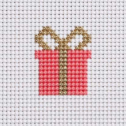 A close-up of a cross-stitch design depicting a red gift box with a gold ribbon and bow, stitched on white mesh fabric.